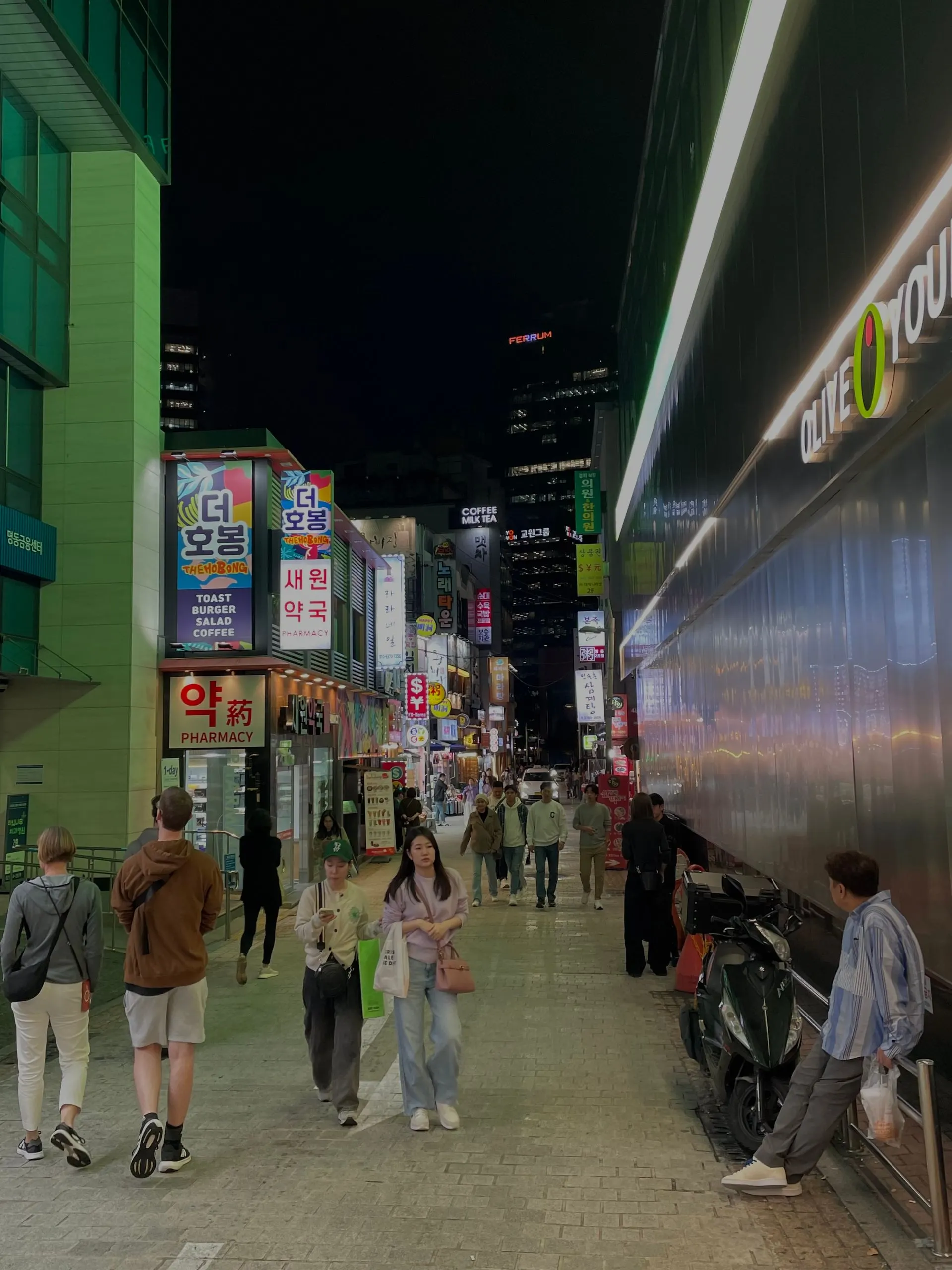 A busy Myeongdong street at night, with bright shop signs and pedestrians.
